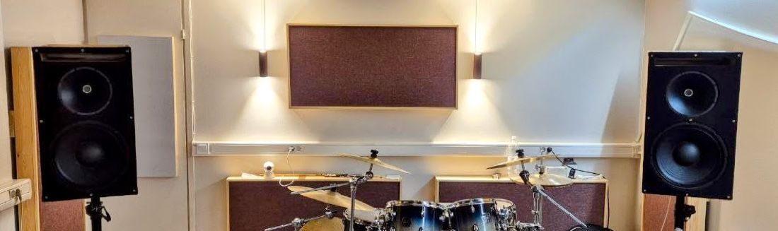 Both PA two-ways on stands flanking the drum kit in the treated rehearsal studio