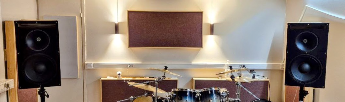 Both PA two-ways on stands flanking the drum kit in the treated rehearsal studio